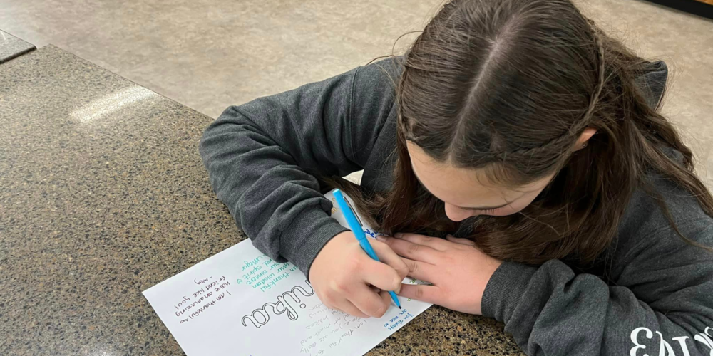 a girl writing a thank you note on a sheet of paper with a blue pen