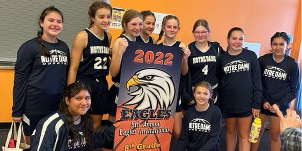 The girls basketball team smiling and holding a banner that declares them winners of the 5th annual Eagles Invitational